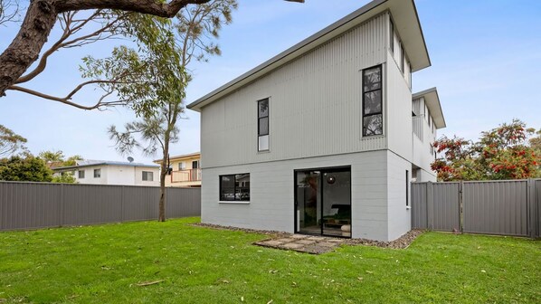 A two-story residential building with a flat roof, a visible garage door, and a small front yard with grass and a tree. - Manyana Beach Escape (Manyana)
