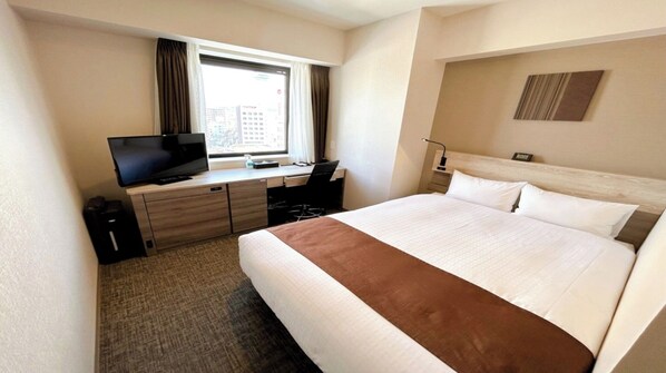 Une chambre d’hôtel avec un lit, un bureau avec une télévision, une chaise et une fenêtre avec des rideaux.