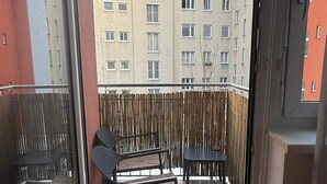 A balcony with two chairs and a table, a bamboo fence, and a view of multi-story buildings. - Central Area 1BR Apartment With Balcony (Vienna)