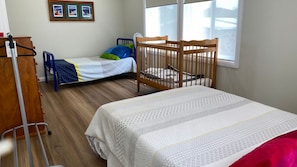 Habitación infantil con una cuna, una cama, un cambiador y una ventana con persianas.