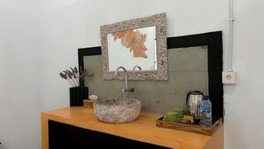 Un baño con tocador de madera, lavamanos de piedra y una obra de arte enmarcada sobre el espejo.