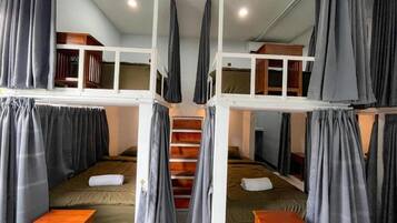 A dormitory-style room with bunk beds, a wooden desk, and a staircase.