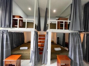 Une chambre de type dortoir, avec des lits superposés, un bureau en bois et un escalier.