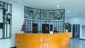 Un mostrador de recepción con dos empleados, una planta decorativa y un letrero que dice 'Happy Christmas'.