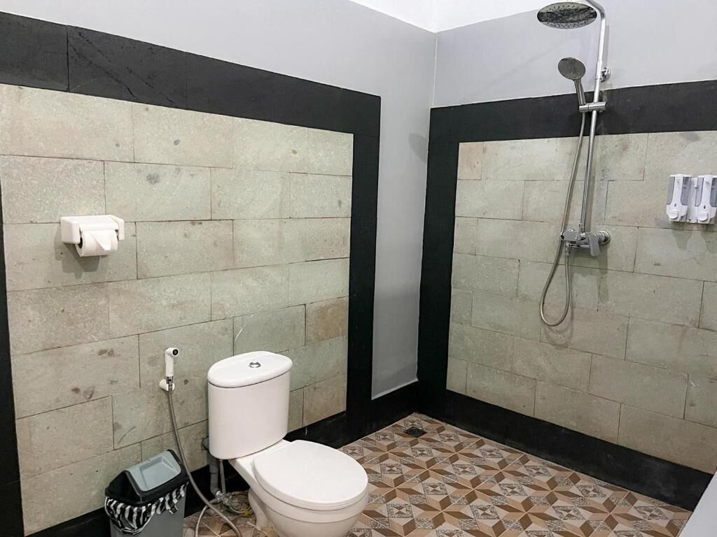 A bathroom with a toilet, a shower, and a trash bin.