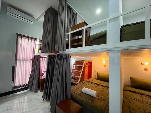 A dorm-style room with bunk beds, a small table, and a window with curtains.