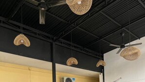 Un amplio comedor interior con mesas y sillas de madera, lámparas de mimbre colgantes y un equipo de aire acondicionado grande en la pared.