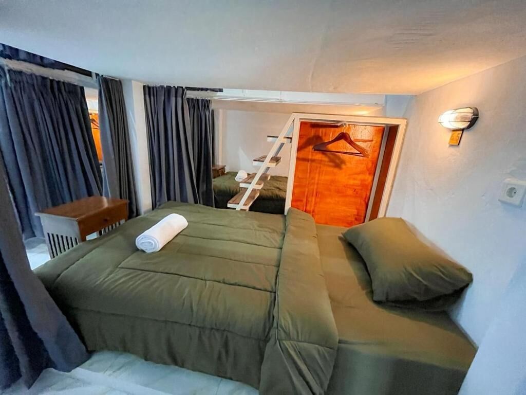 Una habitación compacta con cama, un escritorio pequeño, una silla y una escalera que lleva a una puerta.