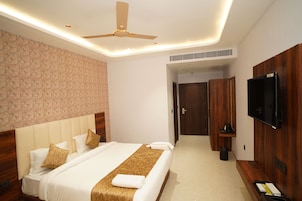 Quarto de hotel com cama, ventilador de teto, televisão e guarda-roupa de madeira.