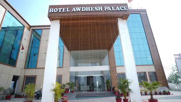 The entrance of Hotel Awdhesh Palace with a modern facade, large glass windows, and potted plants in front. - Avdhesh Palace (Tarabganj)