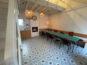 A dining area with a long table, chairs, hanging wicker lamps, a fireplace, and patterned floor tiles.