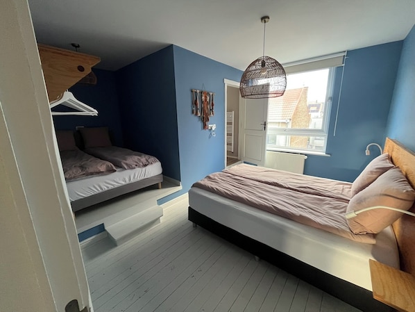 A bedroom with a bunk bed, a hanging light fixture, a window with a view, and a door leading to another room.