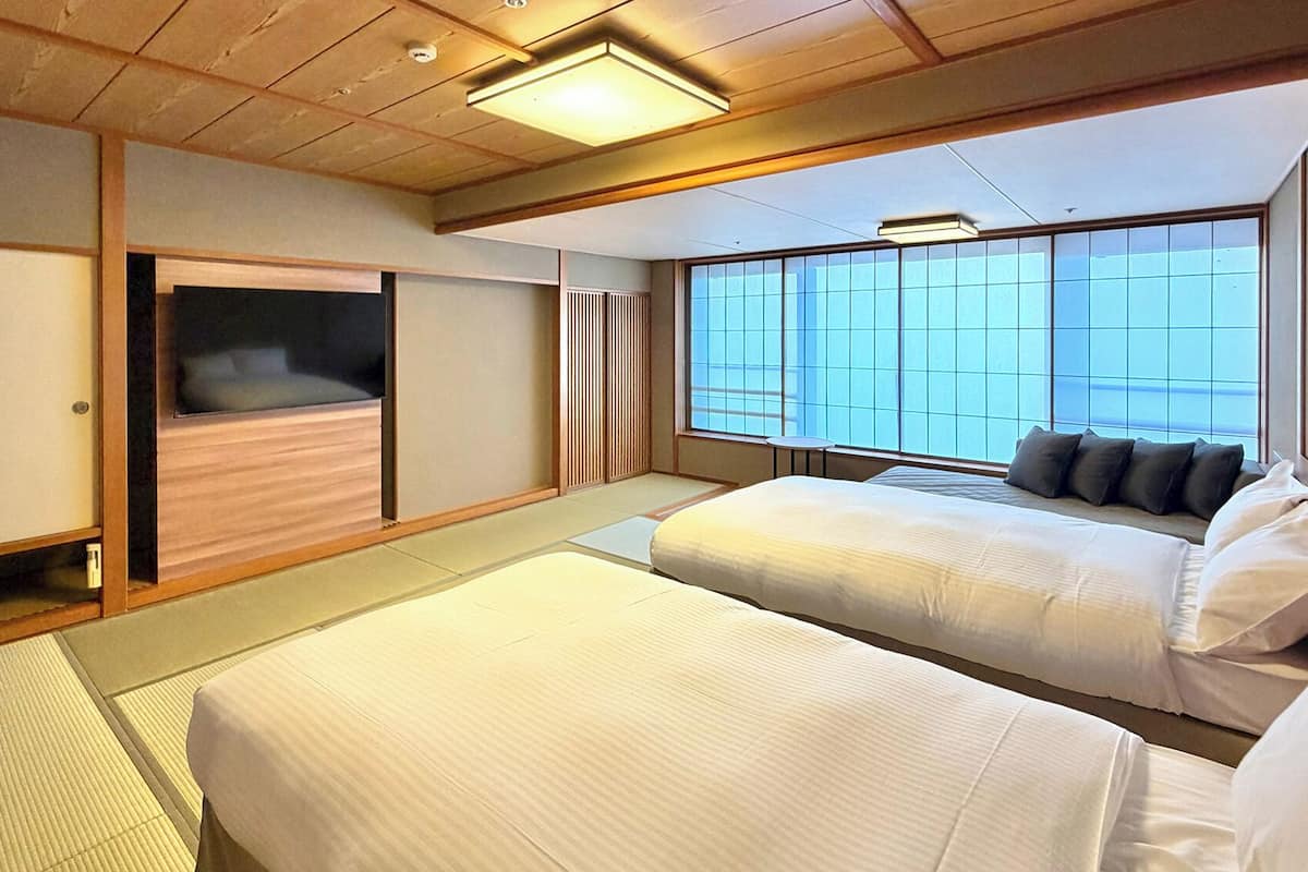 A traditional Japanese-style bedroom with tatami flooring, a sliding door, a bed with pillows, and a large window.