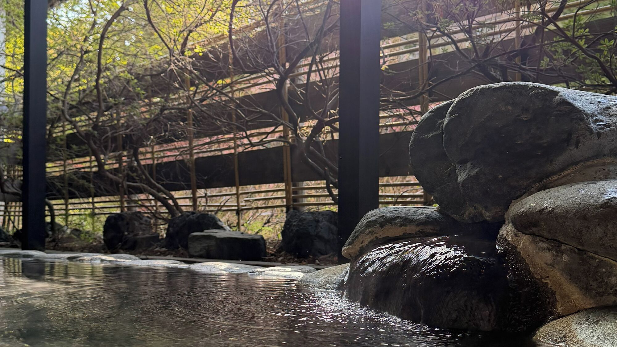 A tranquil outdoor setting with a wooden bridge, large rocks, and a water feature.