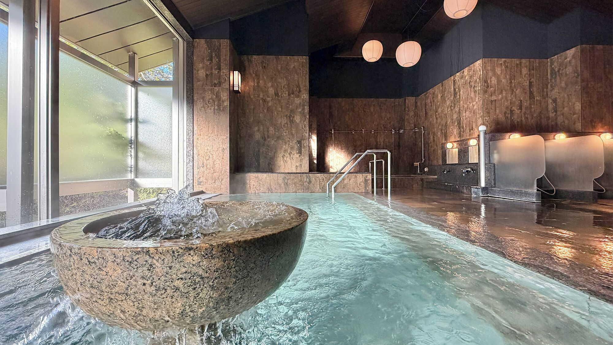 A spa area with a stone hot tub, a glass wall, and a wooden wall with a sauna.