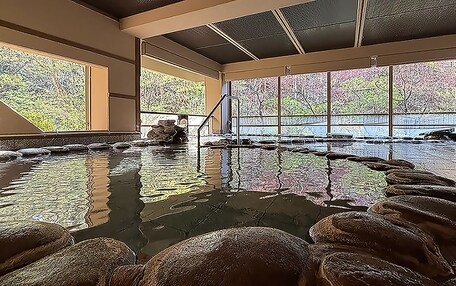 A large indoor pool with clear glass walls, a central water feature, and a stone border.