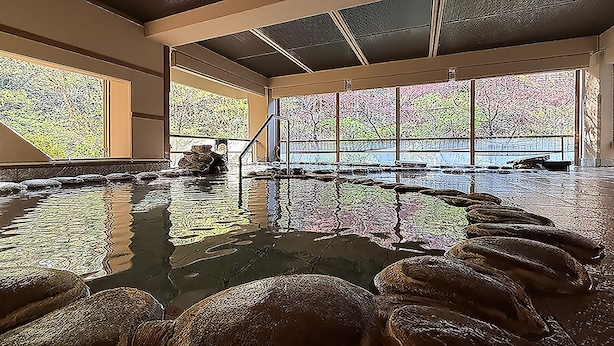 Una amplia piscina interior con paredes de vidrio transparente, un elemento acuático central y un borde de piedra.