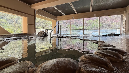 A large indoor pool with clear glass walls, a central water feature, and a stone border.