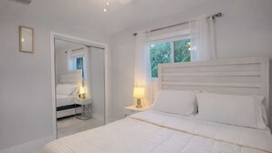 Een slaapkamer met een groot bed, een nachtkastje met een lamp, een spiegel en een raam met gordijnen.