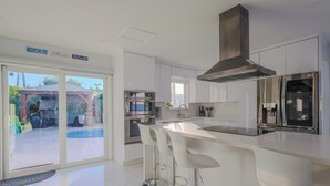 Een moderne keuken met witte kasten, roestvrijstalen apparatuur en een bar voorzien van witte krukken.