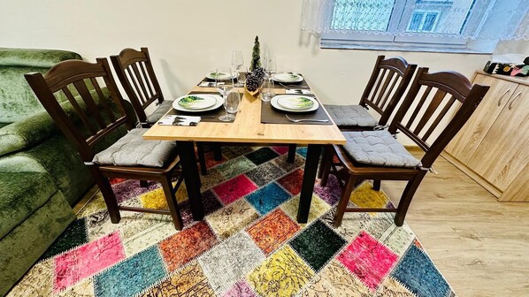 A dining table with four chairs, a colorful patchwork rug, and a window with lace curtains.