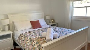 A neatly made bed with a floral bedspread, white headboard, and two bedside lamps. - Nautilus is pet friendly in North Bendalong (Bendalong)
