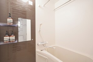 Kylpyhuoneessa on kylpyamme, suihku ja peili. Hyllyllä on pulloja shampoota ja hoitoainetta.