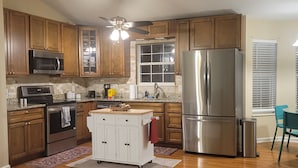 A kitchen with wooden cabinets, a stainless steel refrigerator, a microwave, an oven, a ceiling fan, and a window with blinds. - Mountain view retreat, 3 bedroom overlooking the Foothills. (Maryville)