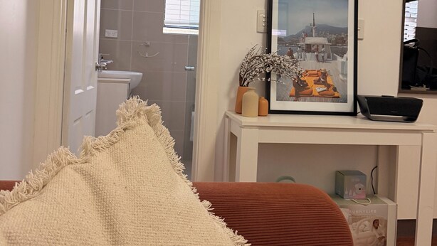 Un salon avec un canapé, un tableau encadré posé sur une console, un ordinateur portable et une boîte étiquetée « SUNNYLIFE ».