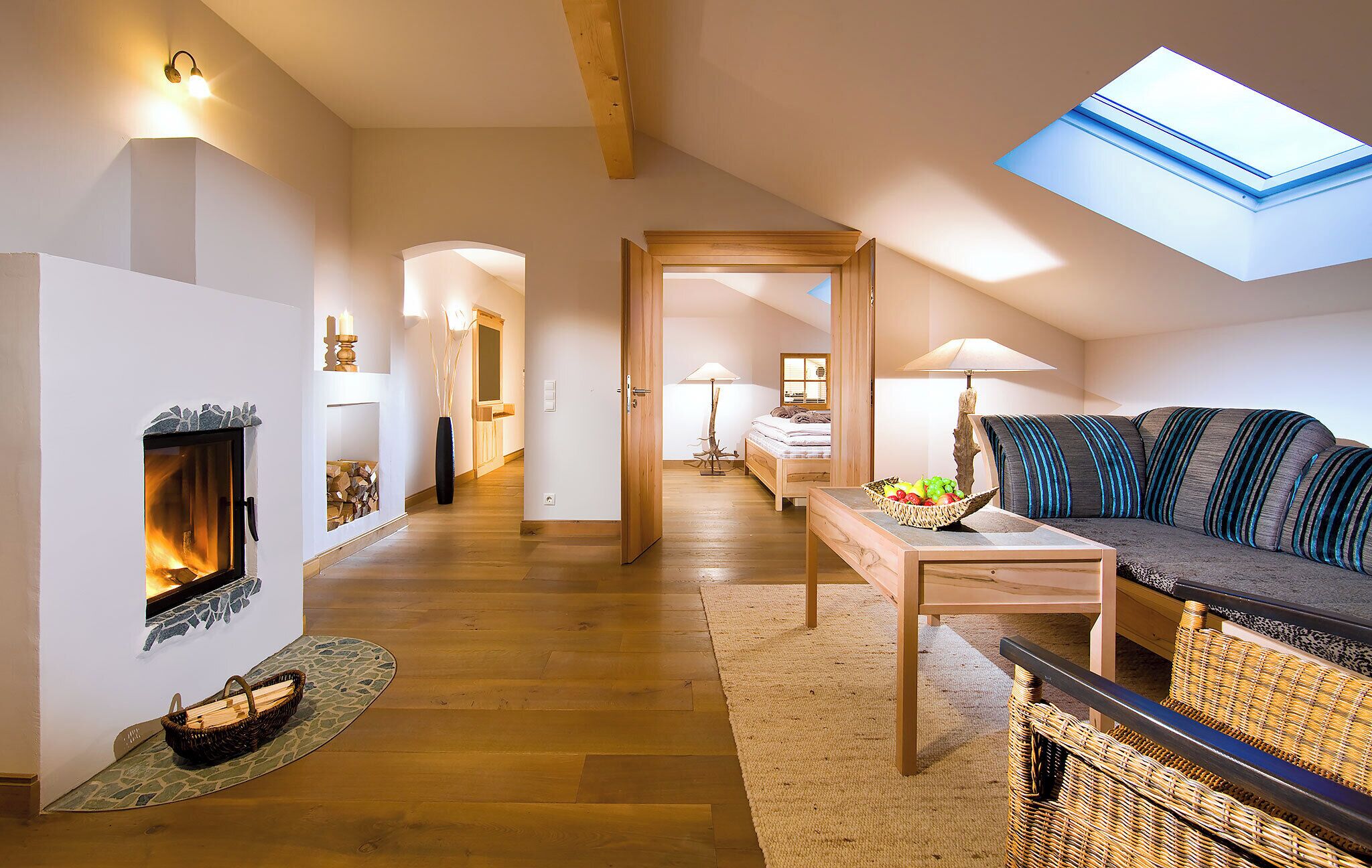 A cozy loft bedroom with a fireplace, a skylight, a bed, and a sofa.