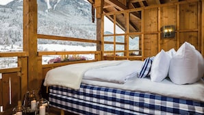 A wooden cabin with a bed, a window with a view of snow-covered mountains, and a candle on the windowsill. - Gams - apartment - balcony with mountain view, fireplace - 65sqm, non-smoking (Ramsau bei Berchtesgaden)