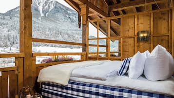 A wooden cabin with a bed, a window with a view of snow-covered mountains, and a candle on the windowsill.