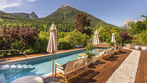 A pool area with lounge chairs and umbrellas, surrounded by lush greenery and mountains. - Gams - apartment - balcony with mountain view, fireplace - 65sqm, non-smoking (Ramsau bei Berchtesgaden)