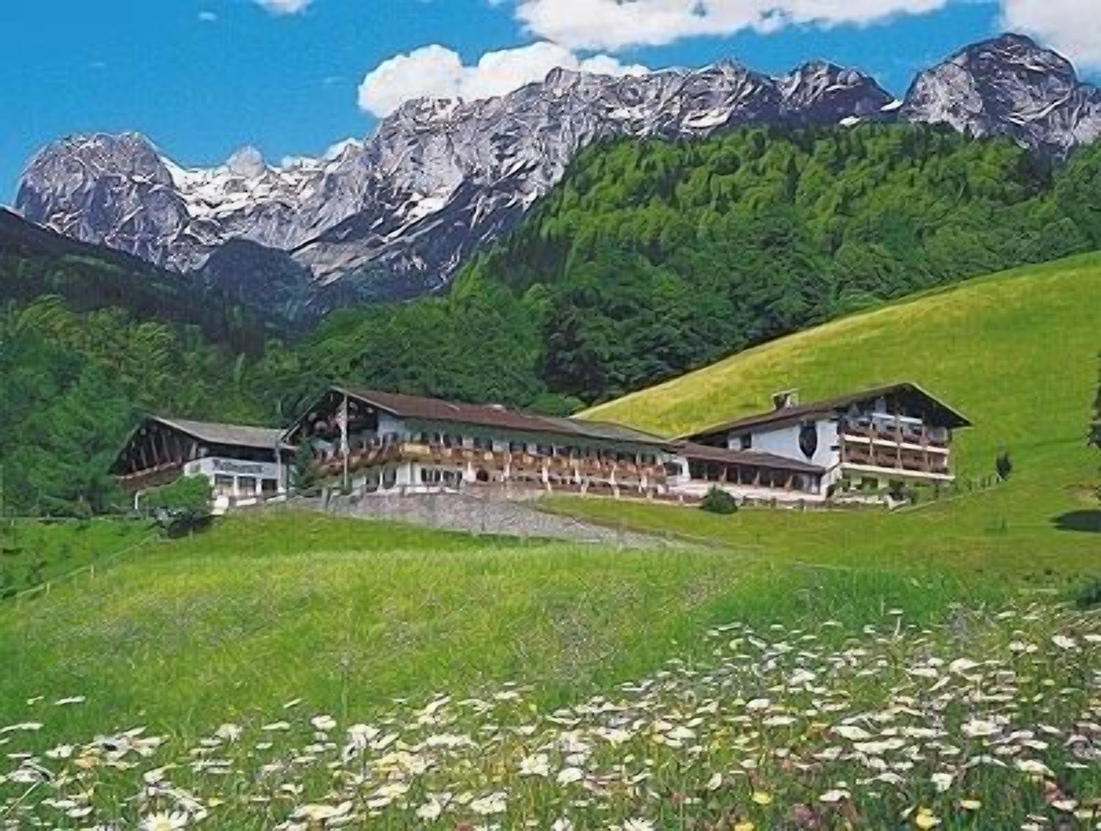 Eine Berglodge mit einem langen, eingeschossigen Gebäude, einer überdachten Außenbereich-Sitzgelegenheit und Blick auf schneebedeckte Berggipfel im Hintergrund.