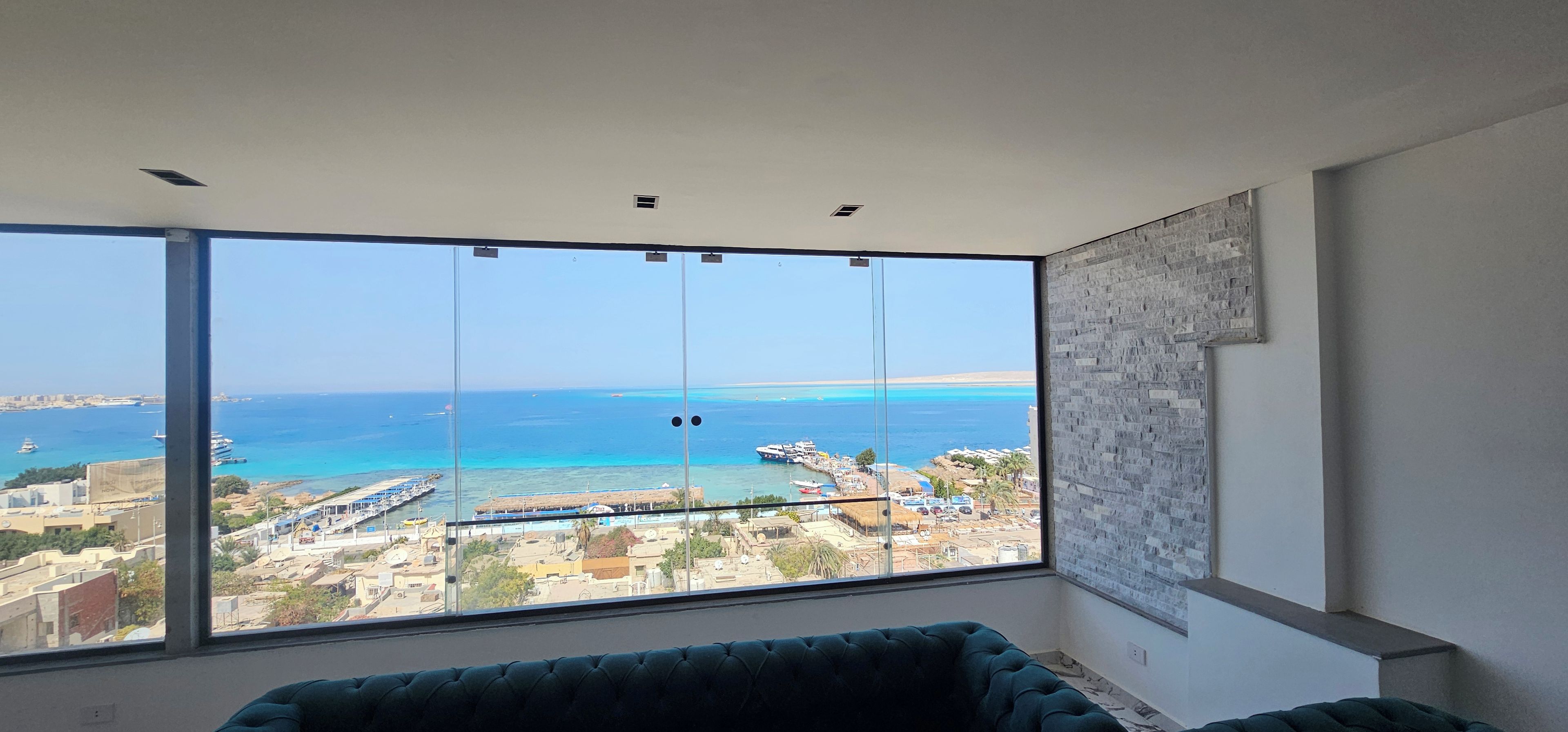 A room with a large window offering a view of the sea and a marina.