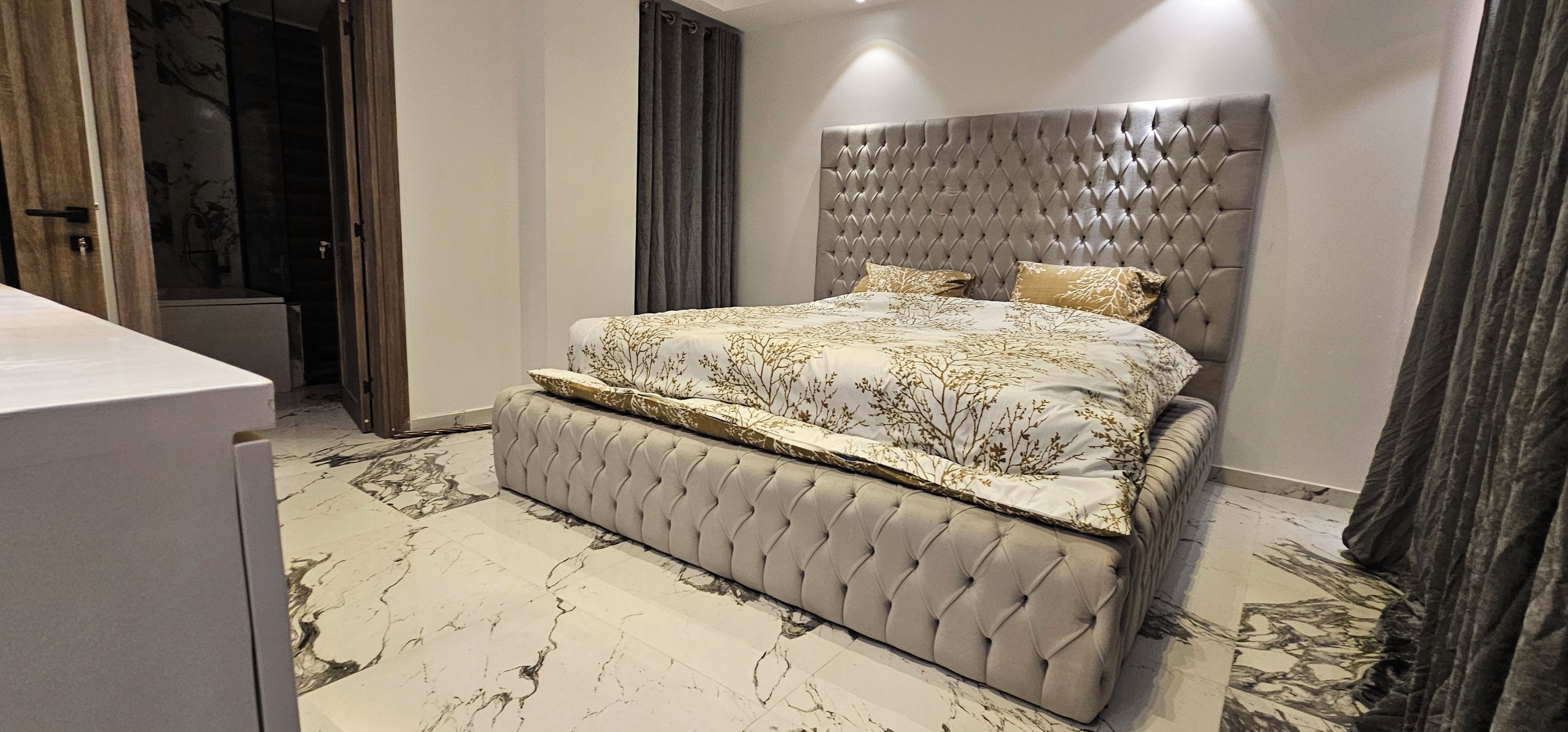 A bedroom with a tufted headboard, a bed with a patterned bedspread, and a marble floor.