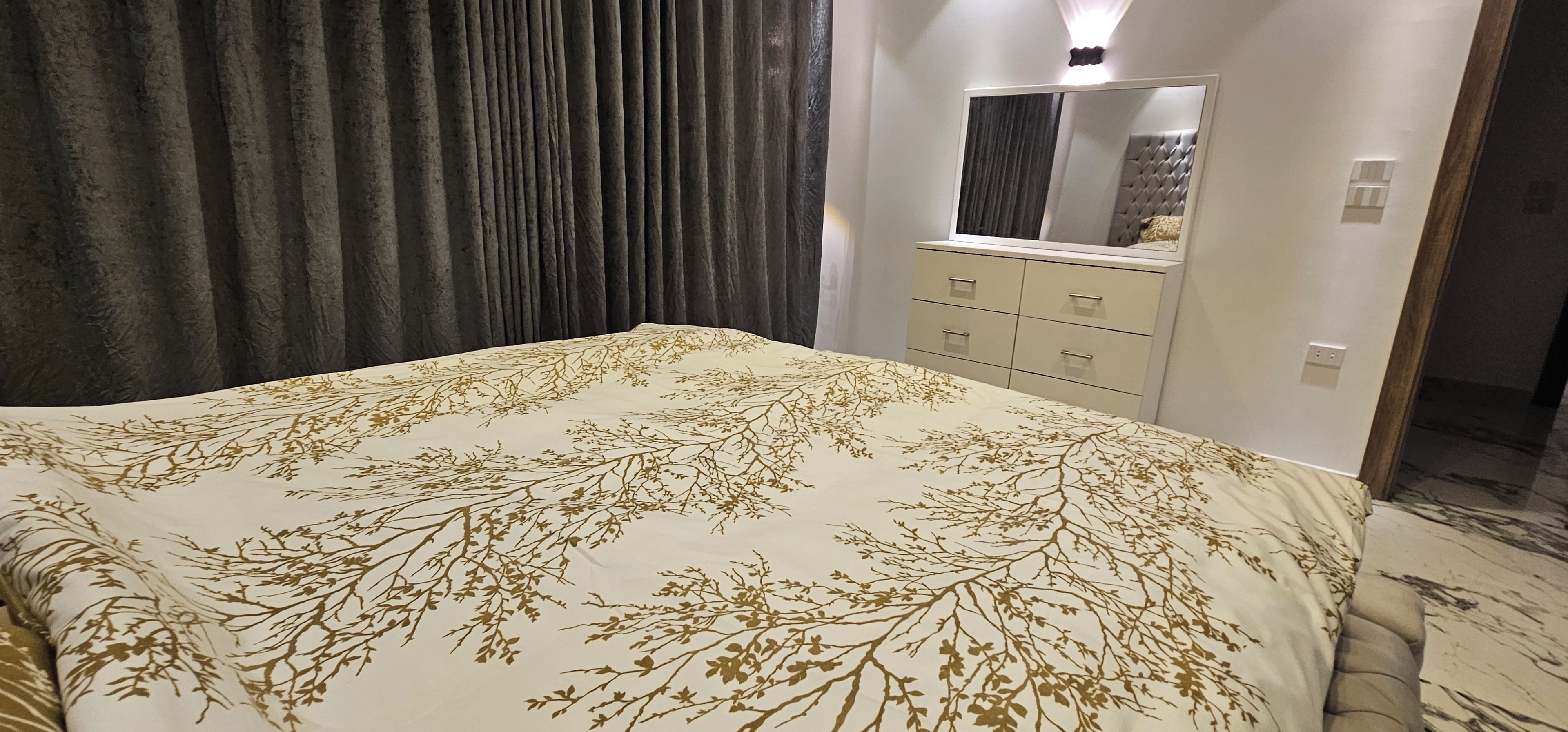 Un dormitorio con cama, cómoda, espejo y cortina.