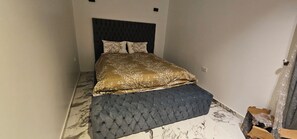 Ein Schlafzimmer mit einem Bett, einem dunklen Kopfteil und einem Boden mit Marmoroptik.