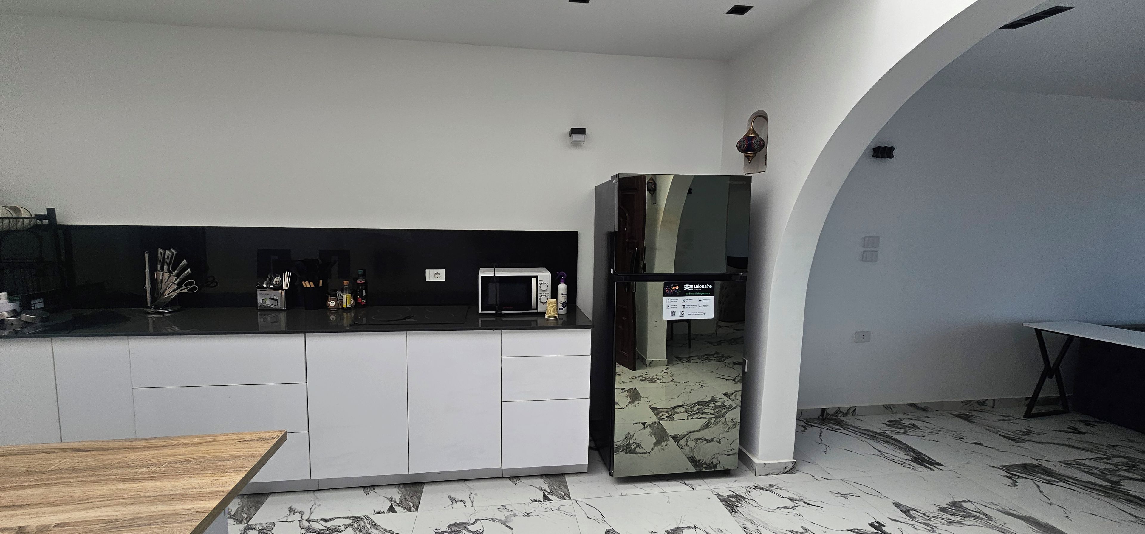 Une cuisine moderne avec des meubles blancs, un plan de travail noir et un sol à motifs de marbre.