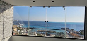 Ein großes Fenster mit Blick auf das Meer, Gebäude und einen klaren Himmel.