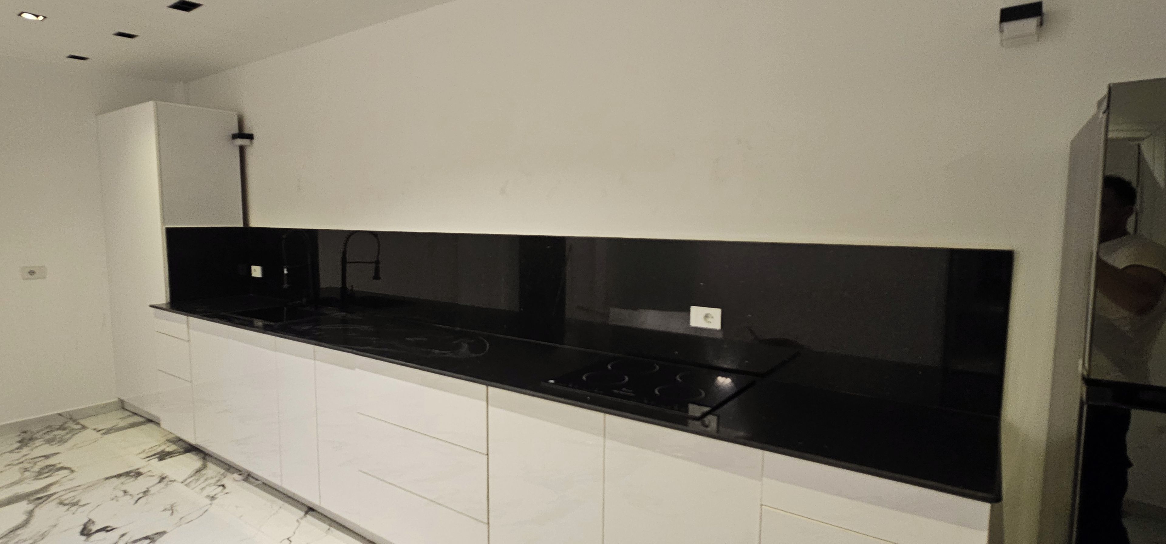 A modern kitchen with a black countertop, white cabinets, and a tiled floor.