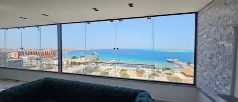 A spacious room with large windows offering a view of a coastal cityscape, including a marina and buildings.