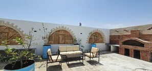 Eine Terrasse mit Gartenmöbeln, einem Backofen aus Ziegeln und dekorativen Gitterfenstern.