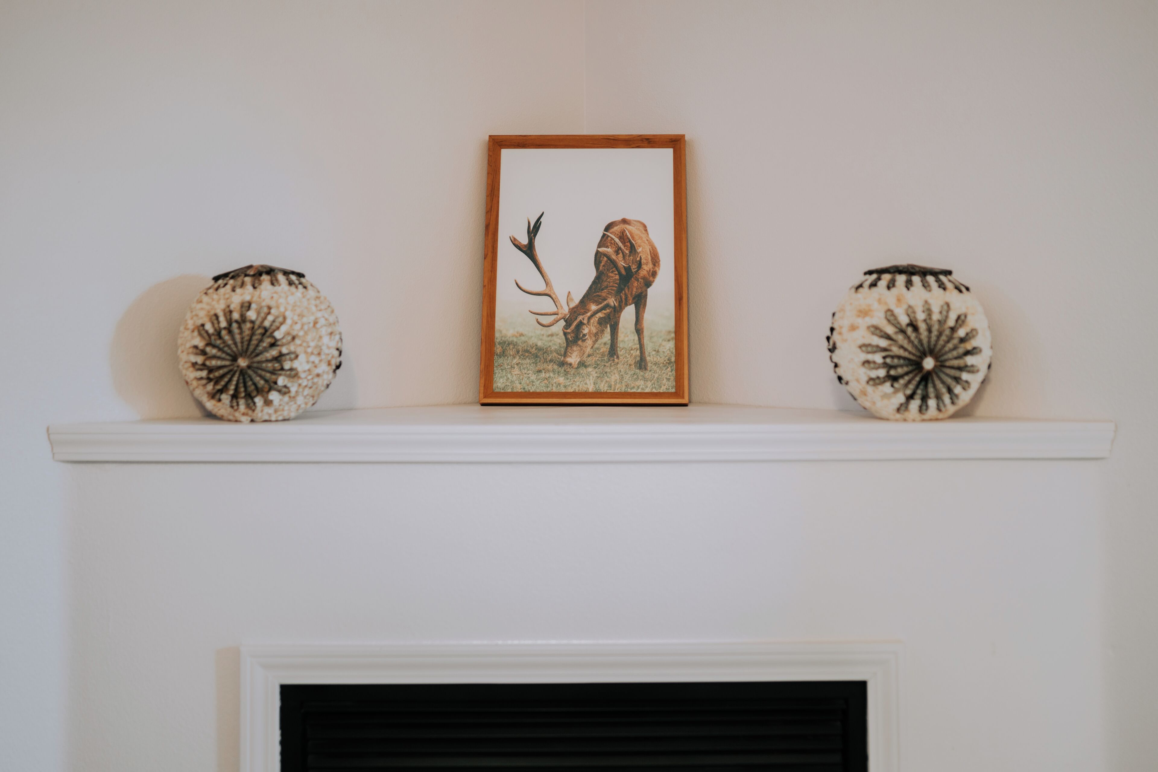 A fireplace with a framed picture of a deer above it, flanked by two decorative vases.
