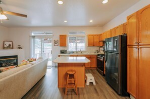 A modern kitchen with wooden cabinets, a black refrigerator, and a central island with a stool.