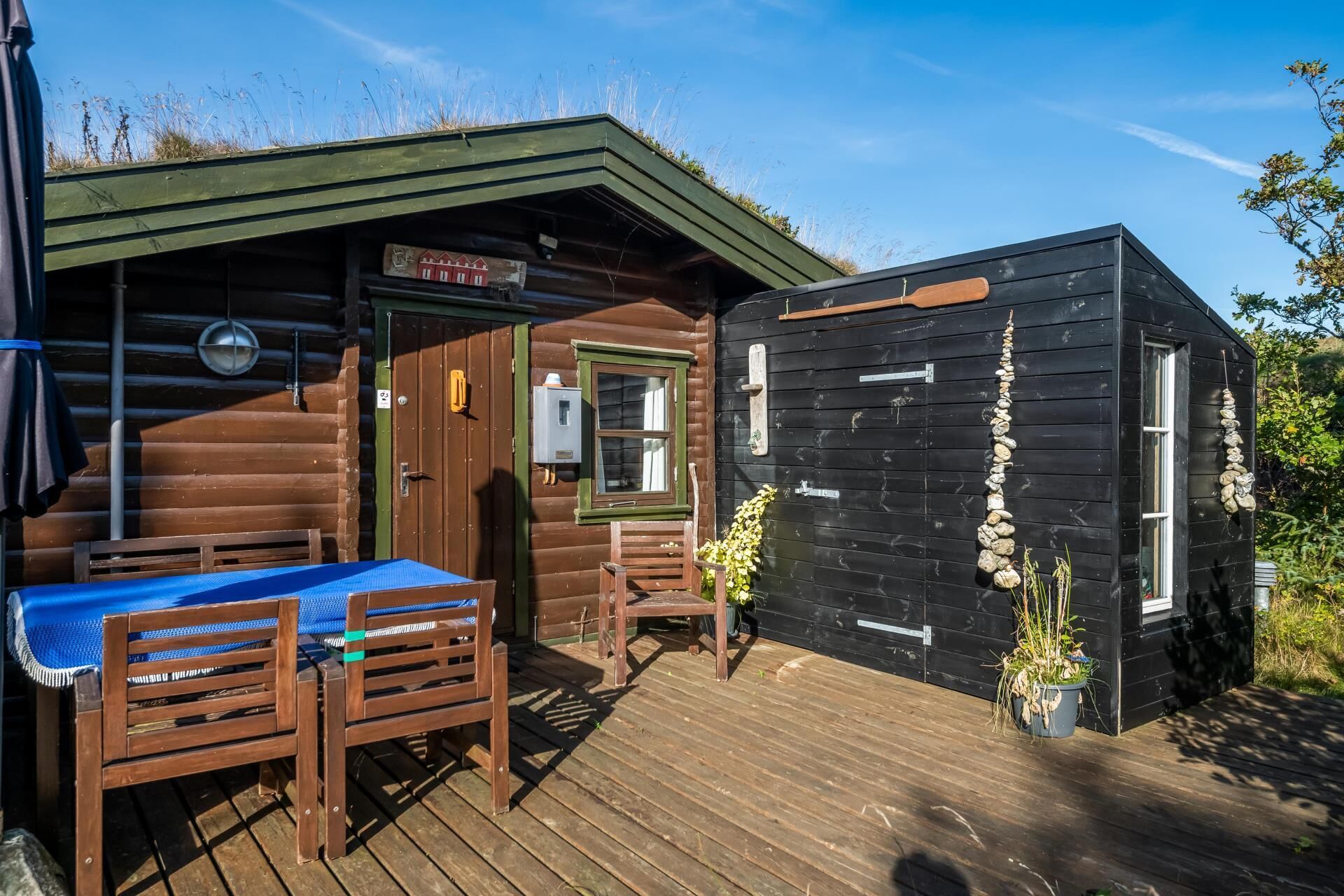 A wooden cabin with a deck, a small table with a blue tablecloth, and a chair.