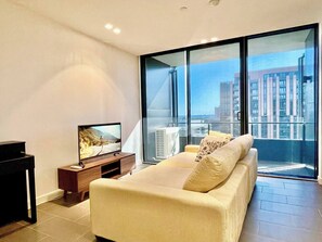 Ein modernes Wohnzimmer mit einer Couch, einem Fernseher auf einem Holzschrank und einem großen Fenster mit Blick auf die Stadt.