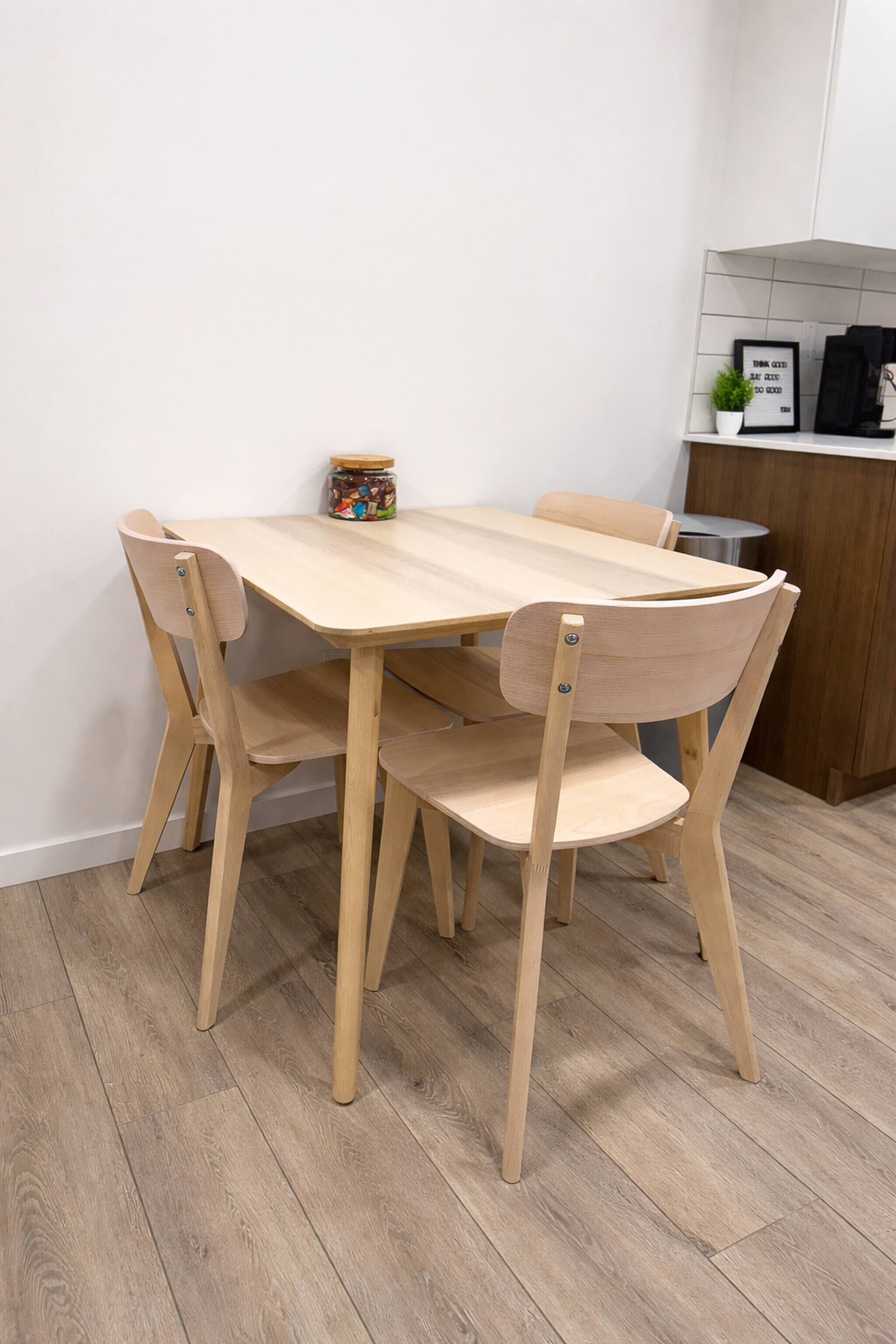 Une table à manger en bois, avec quatre chaises, une petite plante en pot et une citation encadrée accrochée au mur.