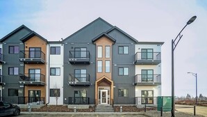 Un immeuble résidentiel à plusieurs étages, doté d’une entrée centrale, de balcons et d’un espace de stationnement à l’avant.