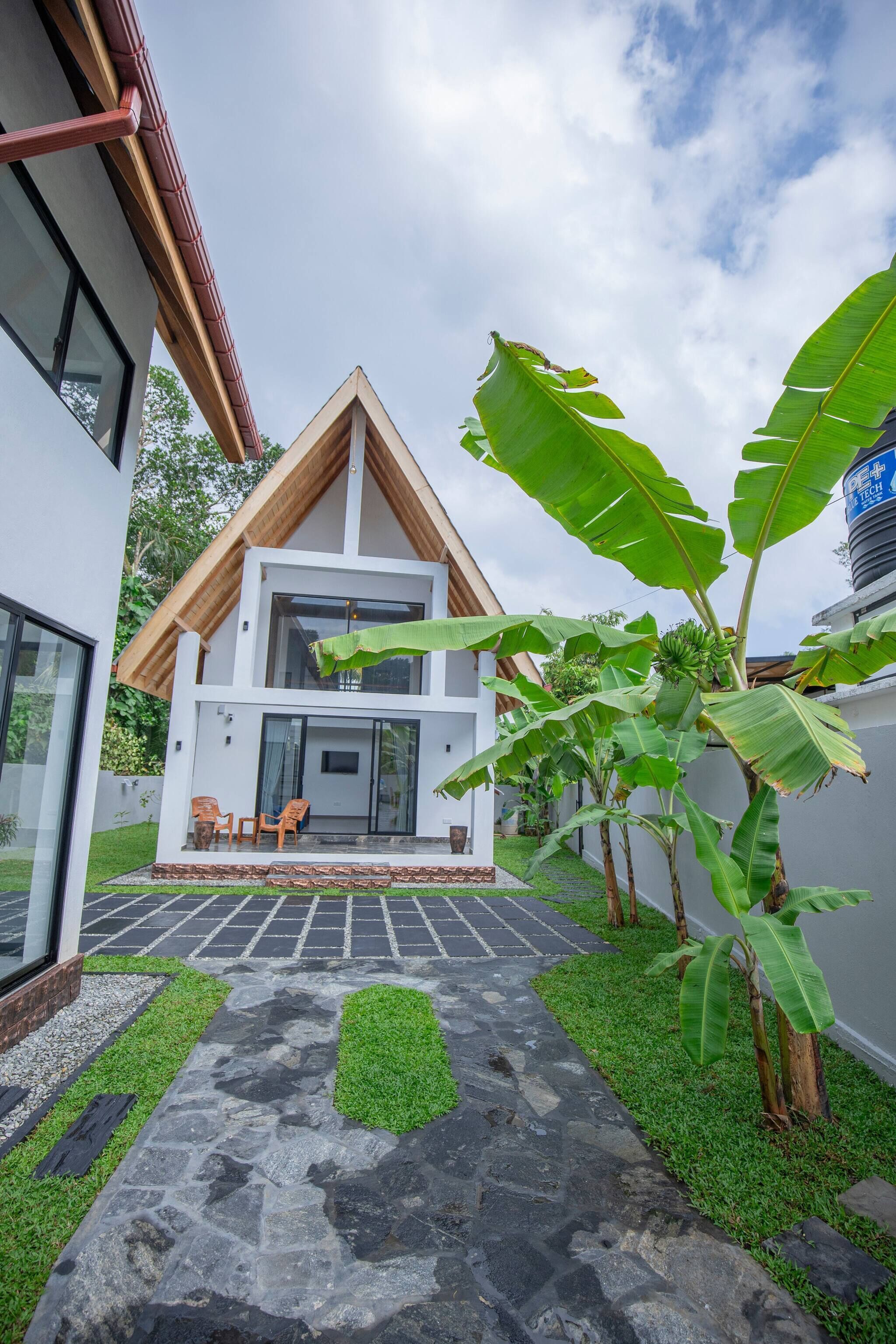 Une maison moderne à deux étages, avec un chemin en pierre et un petit espace patio.